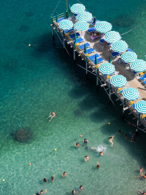 an overhead image of people swimming in the sea next to a skinny bagno on a pier in the bay of naples